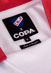 Rood en wit sportshirt met een geweven label met een schildlogo, "C.N. de F." en "COPA," maat S, label met vermelding "Made in Europe."