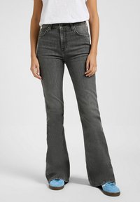 Jeans noirs évasés avec une taille haute et des poches avant. Le tissu a une texture délavée. Assortis à des baskets bleues.