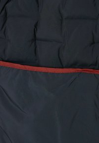 Puffjacke aus dunkelblauem Stoff mit glatter Textur, mit einem roten Akzent im Bereich des Reißverschlusses und sichtbarem Steppmuster.