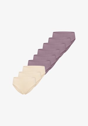 Vrouw met krullend donker haar, een beige draadloze beha en bijpassend ondergoed, kijkt naar links tegen een effen achtergrond.