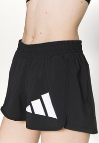 Shorts de sport noirs avec une taille élastique, présentant un design de logo à trois rayures blanches sur le côté gauche et une texture lisse.