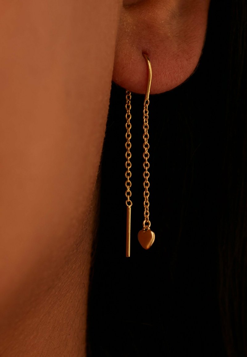 Gold dangling earrings featuring two chains: one with a straight bar and the other with a heart charm, showcasing a smooth finish.