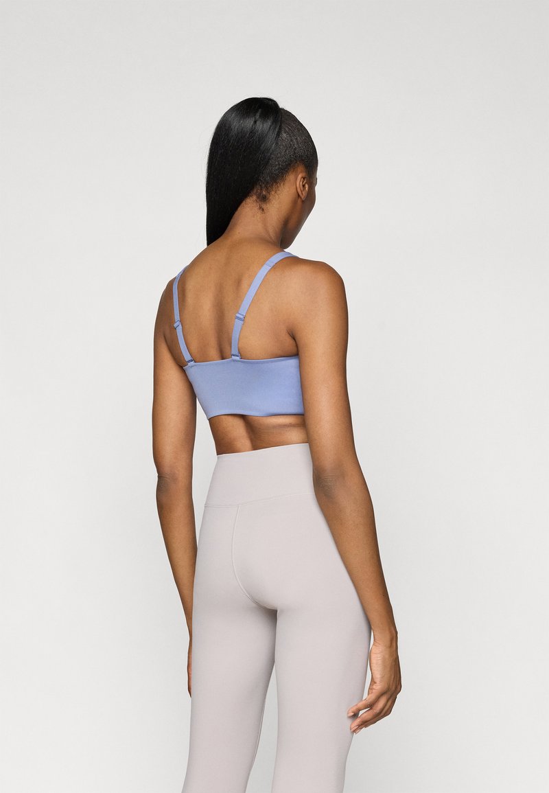Light blue cropped sports bra with adjustable straps, paired with high-waisted beige leggings. Smooth texture, minimal seams.