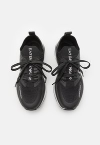 Svarte trening-sko med strikket overdel, tykk gummisåle og kontrastfarge hvit logo. Har tradisjonell snøring og polstret krage.