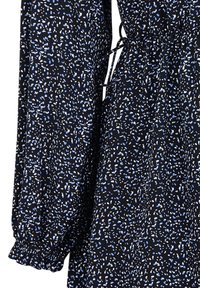 Schwarzes Kleid mit langen, gepufften Ärmeln, das ein verstreutes Muster aus blauen und weißen Punkten aufweist und eine Kordelzug-Taille hat. Weicher, fließender Stoff.