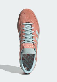 Röd-orange mocka sneakers med ljusblå snören och tre diagonala ränder. Har en vadderad tunga och en mönstrad innersula.