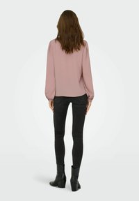 Blusa a maniche lunghe di colore rosa pallido con una finitura texturizzata e maniche a sbuffo, abbinata a jeans neri aderenti e stivali neri alla caviglia.