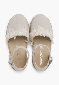 Sandales en tissu beige avec une bordure en dentelle florale, bout rond et une bride de cheville avec une boucle en argent. Tige en toile texturée et semelle naturelle.