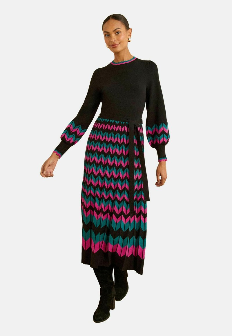 Horgolt ruha hosszú, ballon ujjakkal, fekete felsőrésszel, rózsaszín és türkiz színű cseppfolyós minta a szoknyán, és öv a deréknál.