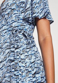 Blå och svart mönstrad klänning med knyt vid midjan, med volangärmar, lättviktig tyg och en lätt lyster.