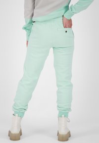 Ljus mynta gröna sweatpants med elastiska mudd och en bakficka med en knapp. Tillverkad av mjukt tyg med en slät yta.