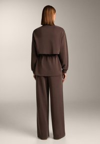 Rjava dvodelna obleka z obrezanim topom z elastiko v pasu in hlačami širokih nog. Mehka tkanina z gladko teksturo.
