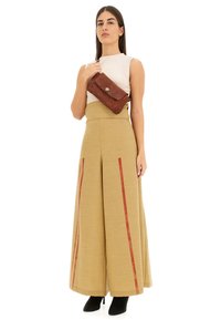 Pantaloni beige a vita alta con strisce rosse, abbinati a una maglietta bianca aderente e una borsa a tracolla in pelle marrone. Tacchi neri completano il look.