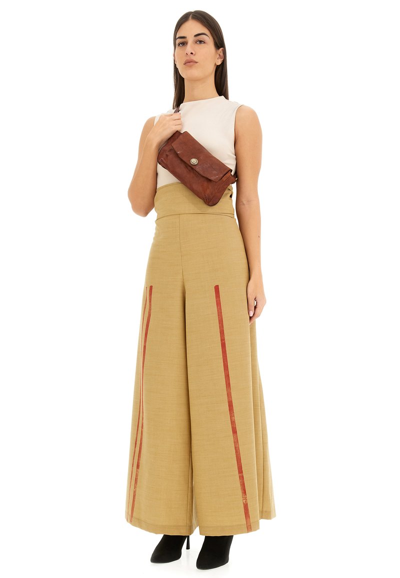 Pantaloni beige a vita alta con strisce rosse, abbinati a una maglietta bianca aderente e una borsa a tracolla in pelle marrone. Tacchi neri completano il look.