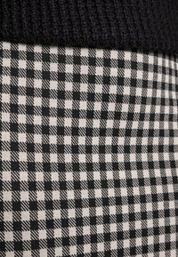 Tissu à carreaux noir et blanc avec des carrés alternant des textures unies et à motifs, présentant une section supérieure en tricot noir.