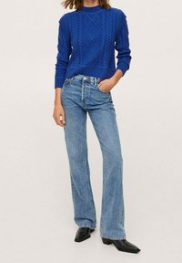 Pull tricoté bleu avec un motif torsadé, associé à un jean évasé bleu clair. Des bottes noires à bout pointu complètent la tenue.