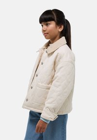 Veste beige matelassée avec un col en velours côtelé, des boutons-pression et une poche frontale. Présente une coupe décontractée et des coutures visibles.