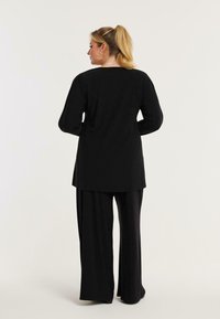 Schwarzes Langarmoberteil mit lockerer Passform, kombiniert mit lässigen schwarzen Hosen. Weicher Stoff, glatte Textur und einfaches Design.