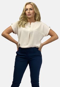 Luźna różowa bluzka z podwiniętymi rękawami, okrągłym dekoltem i guzikami, w zestawieniu z dopasowanymi granatowymi spodniami.