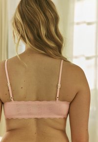 Roza bralet s teksturiranim, rebrastim dizajnom, čipkastim rubom i podesivim trakama s zlatnim detaljima. Pogled s leđa.