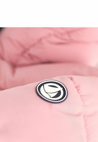 Pink puffer jacket detail featuring a soft, quilted texture. Includes a circular logo badge with a white emblem outlined in navy.