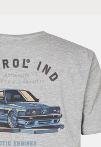 Camiseta de manga corta gris claro con un gráfico de coche azul, texto "Control Ind" y marca de piezas de motor en negro y verde.