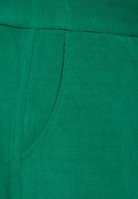 Grön kordflamsväv med vertikala ribbor, en texturerad yta och en sidficka sydd med en kontrasterande söm.