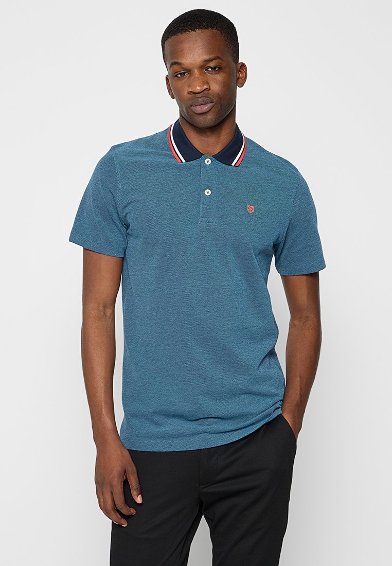 Polo azul hecho de tela texturizada. Presenta un cuello marino con acentos rojos, tres botones y un pequeño logo en el pecho.