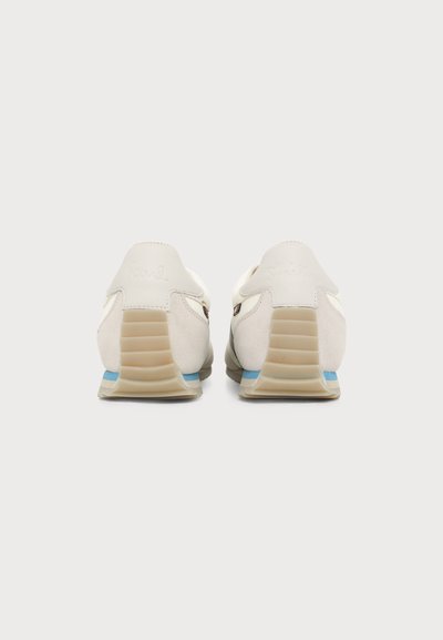 Paire de baskets blanc cassé avec des talons beige côtelés et une fine bande bleue au-dessus de la semelle, vues de dos sur un fond uni.