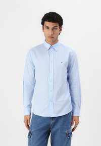 Camisa de botonadura en azul claro, fabricada en algodón. Presenta un cuello clásico, mangas largas y un pequeño logo en el pecho. Corte entallado.