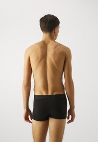 Schwarze Boxer-Shorts haben eine enganliegende Passform und einen elastischen Bund. Der Rücken des Models ist sichtbar, wobei ein glatter, leicht muskulöser Rücken zur Geltung kommt.