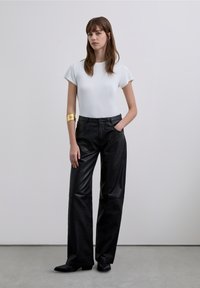 White short-sleeve fitted top paired with high-waisted black leather wide-leg trousers; model wearing a gold cuff bracelet.