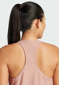 Lichtroze mouwloze sport tanktop van een textuurstof, met een open rugontwerp en een zachte halslijn.