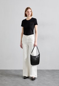 Musta slim-fit t-paita taskulla, valkoiset leveälahkeiset farkut, musta nahkakäsilaukku ja mustat tasapohjaiset kengät mallin päällä neutraalilla taustalla.