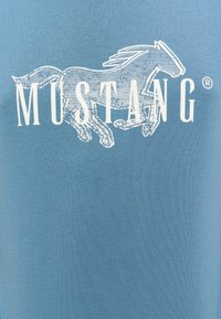 T-shirt en coton bleu avec un graphique blanc d'un cheval courant et le mot "MUSTANG" en lettres gras. Texture douce, design à col rond.