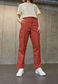 Beige gestreepte t-shirt gecombineerd met hoogwaist oranje broek. Flat-front ontwerp, zakken en witte sneakers. Soepele stof en gestructureerde pasvorm.