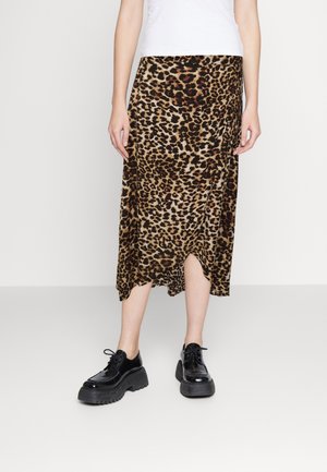 Frau trägt einen Leopardenmuster-Midirock mit einem Frontschlitz und schwarze Plateaulaufschuhe mit Schnürung, steht vor einem schlichten weißen Hintergrund.