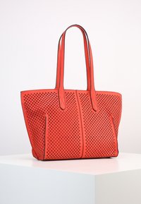 Sac fourre-tout rouge perforé avec des accents noirs, en forme rectangulaire, double poignées et un design ouvert présentant des motifs étoilés.