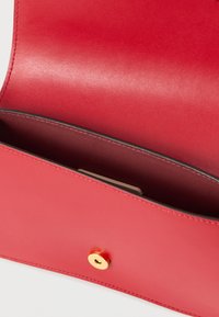 Interno di borsa a tracolla in pelle rossa con texture liscia, dotato di chiusura a scatto in metallo dorato e fodera con tasca profonda.