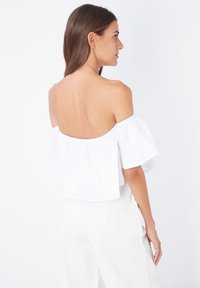 Top blanco sin hombros con mangas cortas y volantes; tejido ligero; diseño cropped. Textura lisa, estilo minimalista, sin patrones.