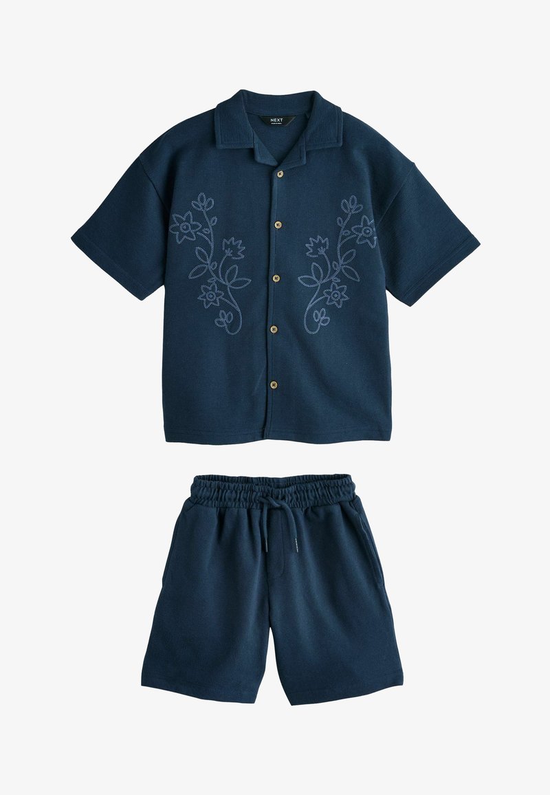 Chemise bleu marine à manches courtes avec boutons et broderie florale, associée à un short bleu marine à taille élastique avec cordon de serrage.