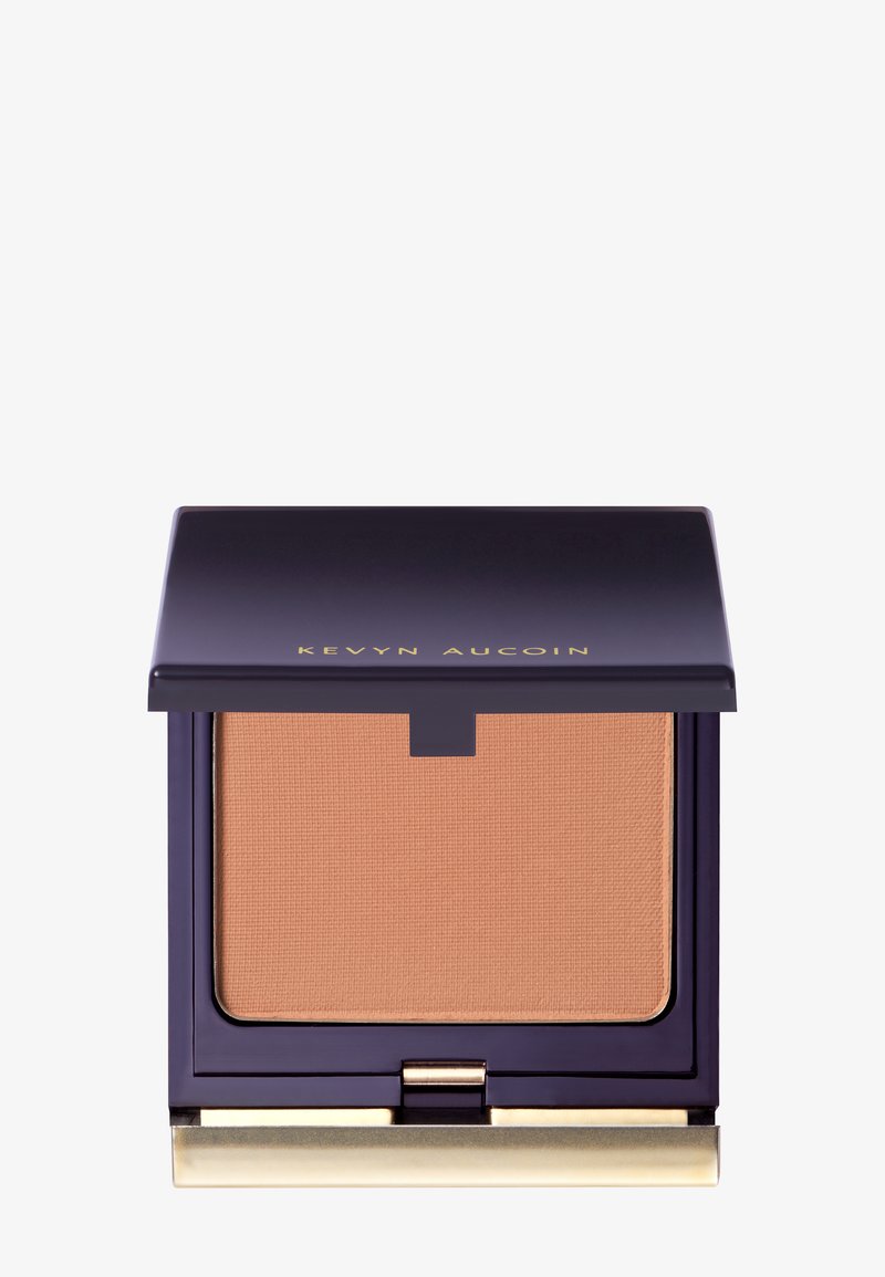 Poudre compacte dans un étui carré de couleur violet profond avec un accent doré. La poudre a une surface texturée dans une teinte beige chaud.