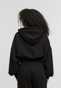 Zwarte cropped hoodie met een trekkoord kap, lange mouwen en een relaxte pasvorm. Zachte stof en naadloos achterkantontwerp. Gecombineerd met zwarte joggers.