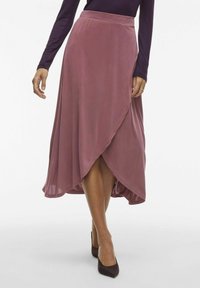 Jupe enveloppante mauve en tissu doux, avec un design fluide et un ourlet asymétrique, associée à des escarpins noirs à bout pointu.