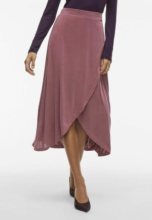 Jupe enveloppante mauve en tissu doux, avec un design fluide et un ourlet asymétrique, associée à des escarpins noirs à bout pointu.