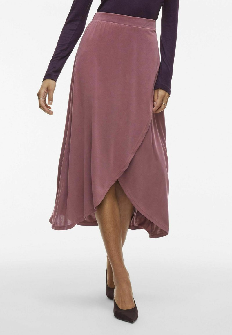 Jupe enveloppante mauve en tissu doux, avec un design fluide et un ourlet asymétrique, associée à des escarpins noirs à bout pointu.