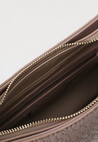 Sac à main en cuir marron texturé avec fermeture éclair. L'intérieur présente une doublure lisse et plusieurs compartiments pour l'organisation.