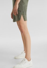 Olive green cotton dress with side slits and tonal stitching. Paired with white sneakers featuring a classic design and textured surface.