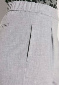 Lichtgrijze elastische taillebroek met zij- en achterkantzakken, gedragen met een zwart-wit gemusterd kledingstuk bovenaan.
