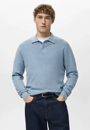 Polo bleu clair à manches longues avec une finition texturée, col à boutons et coupe cintrée, associé à un jean en denim foncé et une ceinture noire.